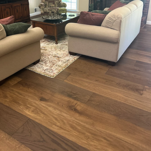 A living room features plush sofas and a patterned rug on a rich, dark hardwood floor.